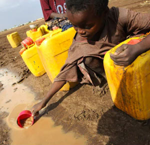 A child collecting muddy water with a cup to fill a yellow jug